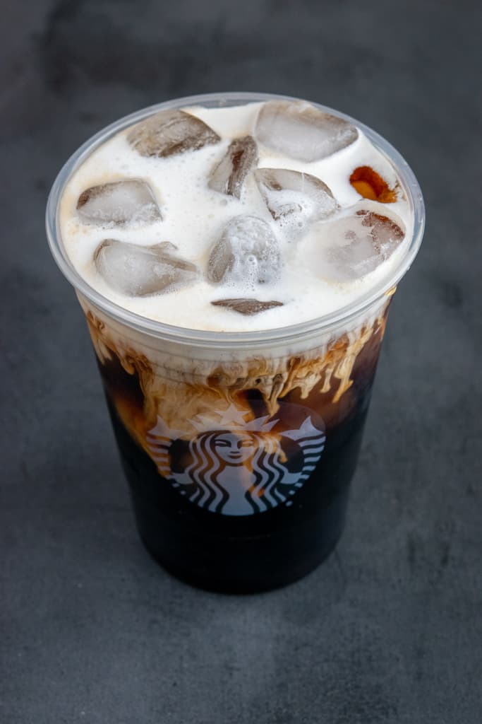 Sweet cream flowing into cup of cold brew.