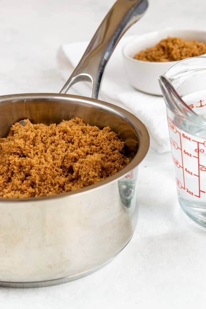 Saucepan full of brown sugar and measuring cup with water.