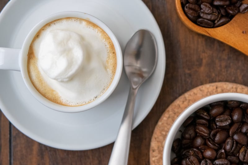 Espresso topped with whipped cream in white cup with spoon on saucer.