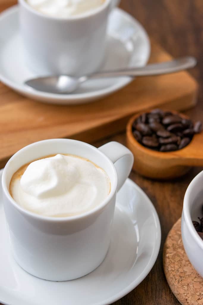 Espresso con panna in white demitasse cup and saucer and scoop of coffee beans.