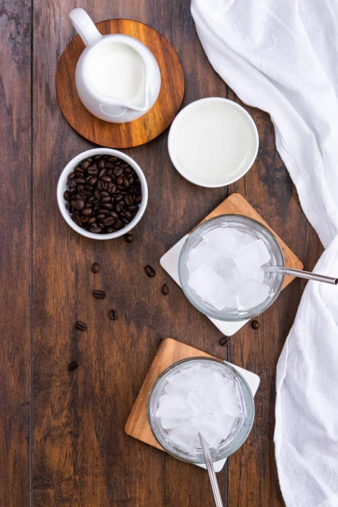 two cups filled with ice and straws and bowl of coffee beans