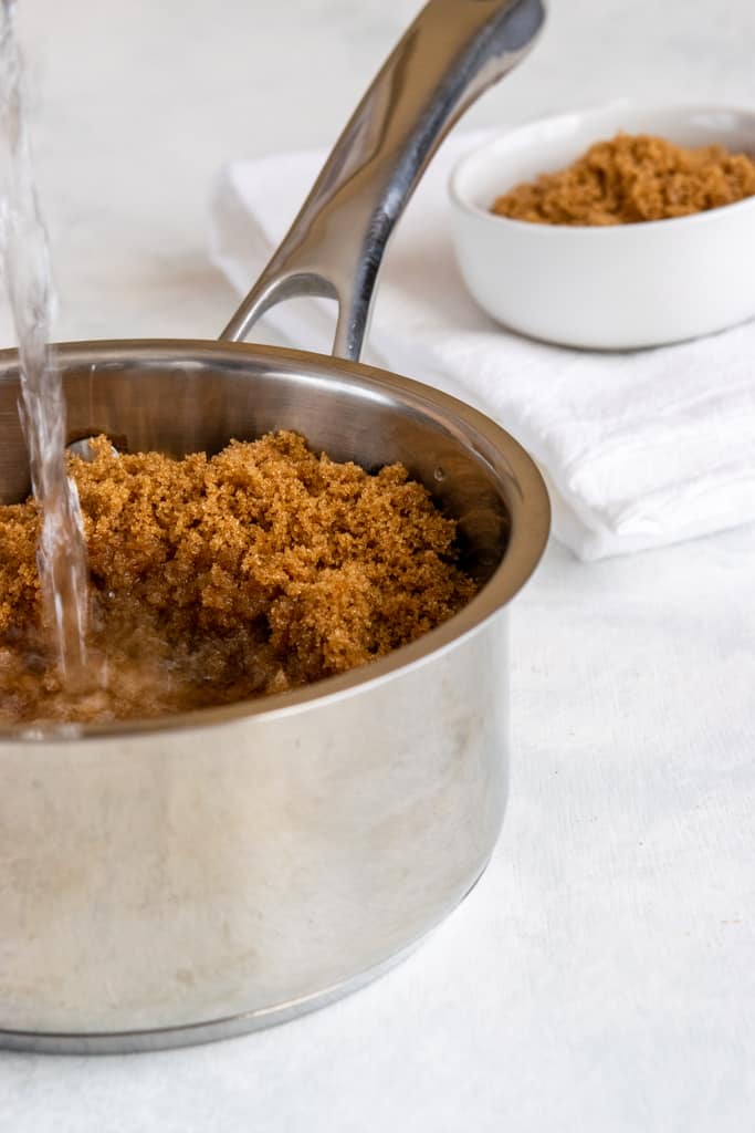 Making brown sugar syrup by pouring water into pan with sugar.