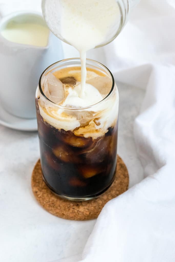 pouring vanilla sweet cream into glass of ice and cold brew coffee