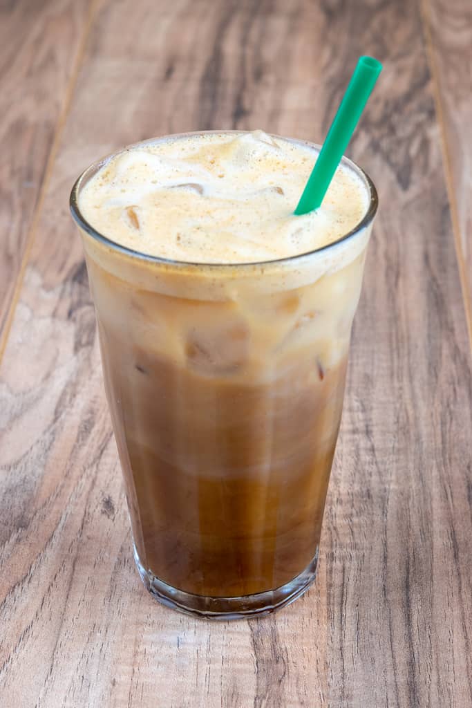 Copycat Starbucks Iced Brown Sugar Oatmilk Shaken Espresso stirred together in glass with a green straw.