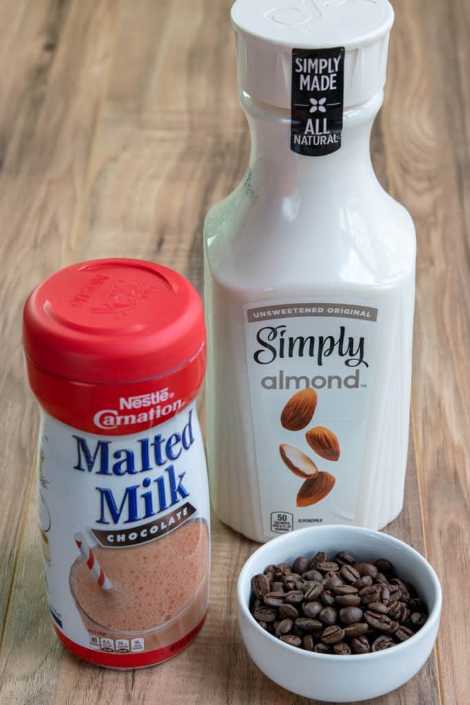 Carnation chocolate malted milk, bottle of almond milk and blonde roast coffee beans.