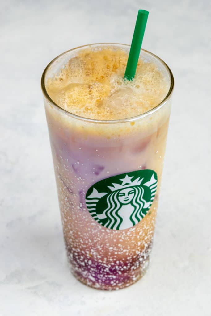 Foamy and layered Iced Shaken Espresso in glass with Starbucks logo and green straw.