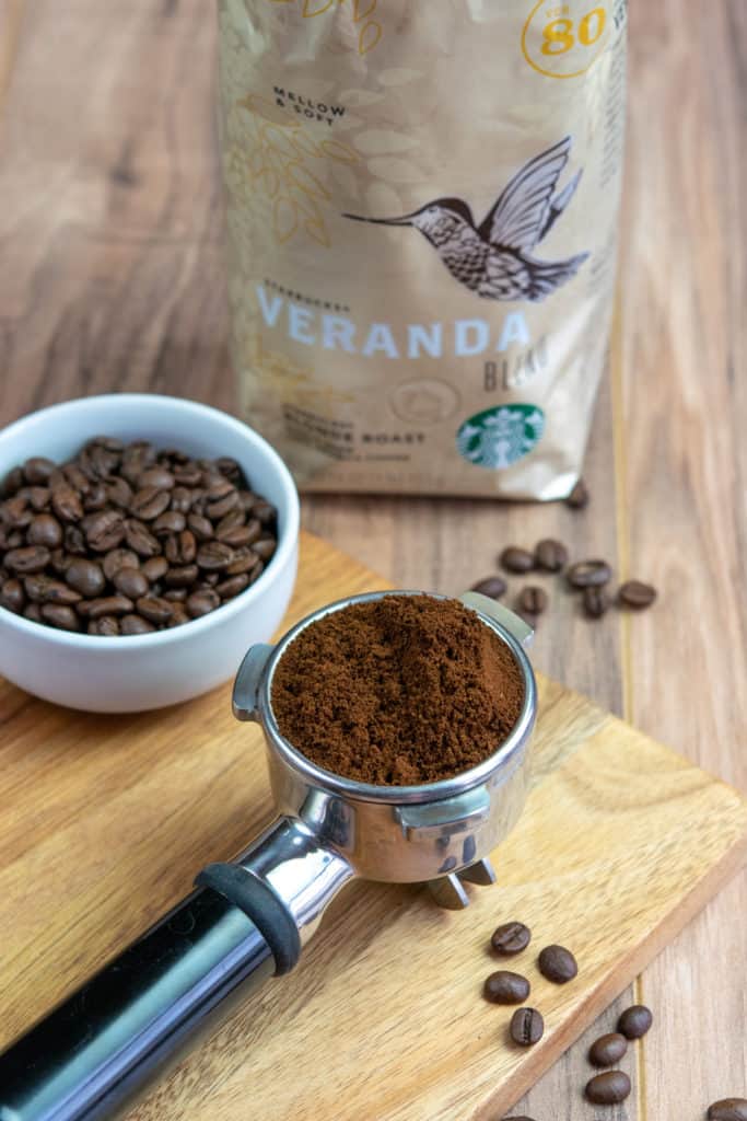 Bag of Starbucks Veranda blonde roast coffee beans and espresso portafilter with ground coffee in it.