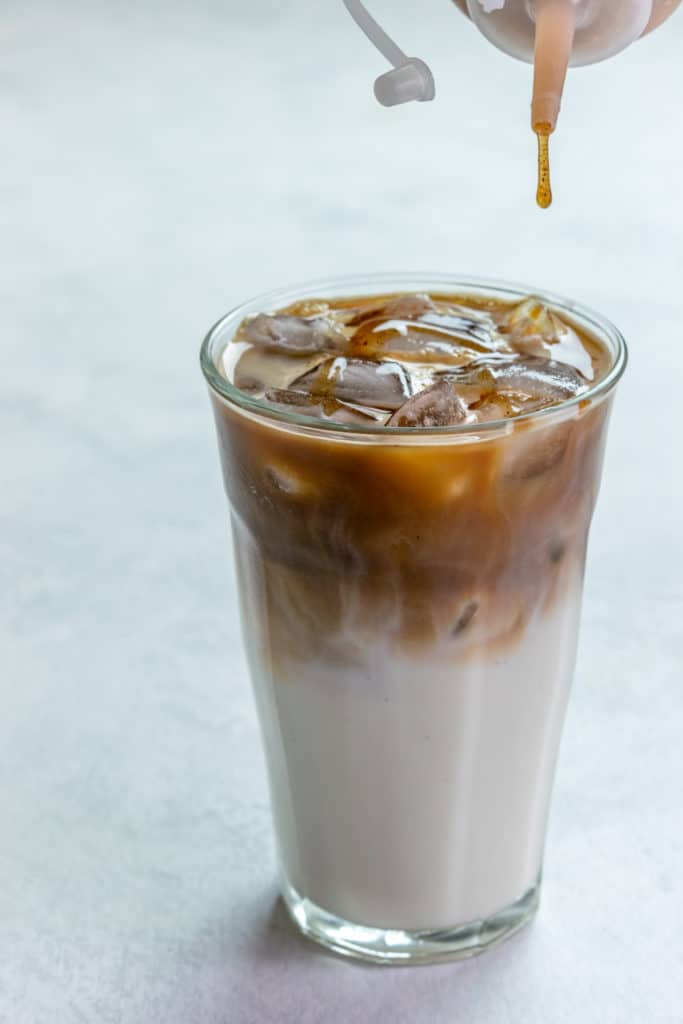 Spiced Apple Drizzle being squeezed on top of iced macchiato.
