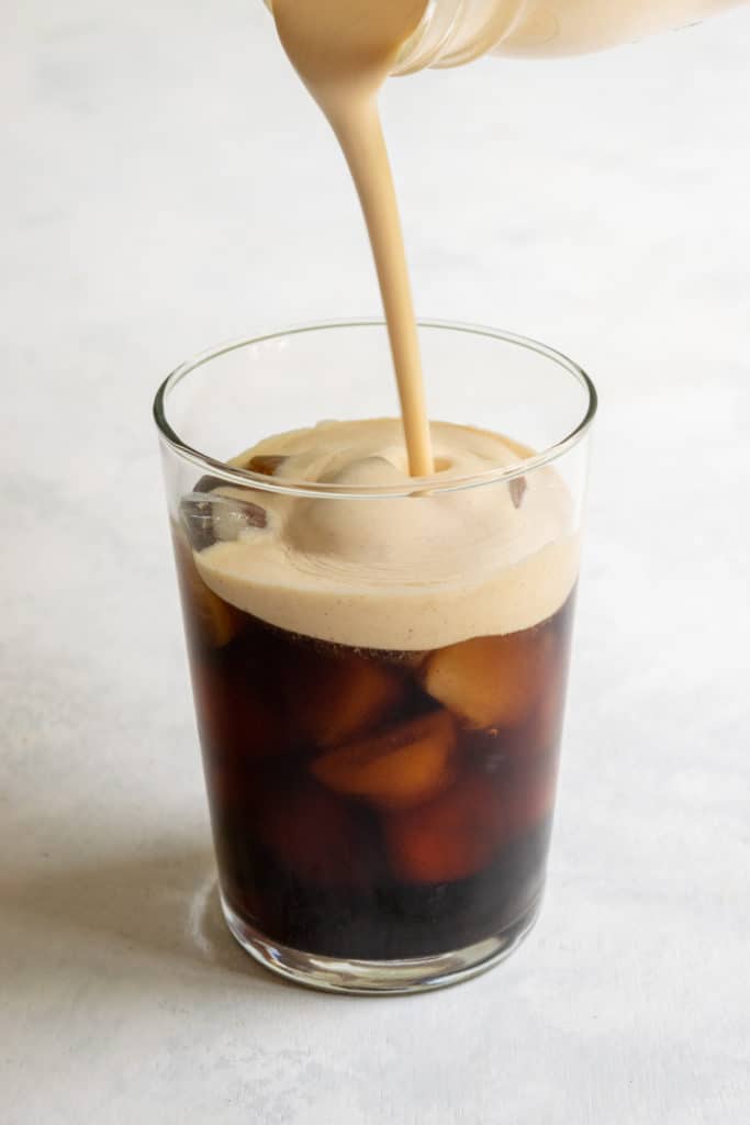 Pouring homemade pumpkin cream cold foam on top of cold brew coffee.