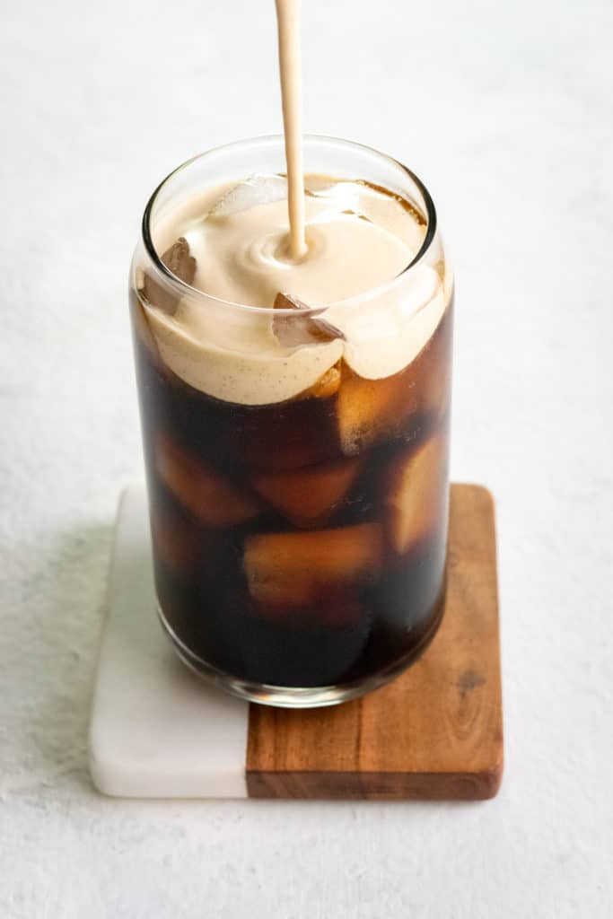 Pouring pumpkin cream topping on an iced cold brew coffee drink.