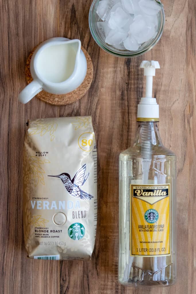 Bag of blonde roast espresso, bottle of Starbucks vanilla syrup, milk and ice for making an iced blonde vanilla latte.
