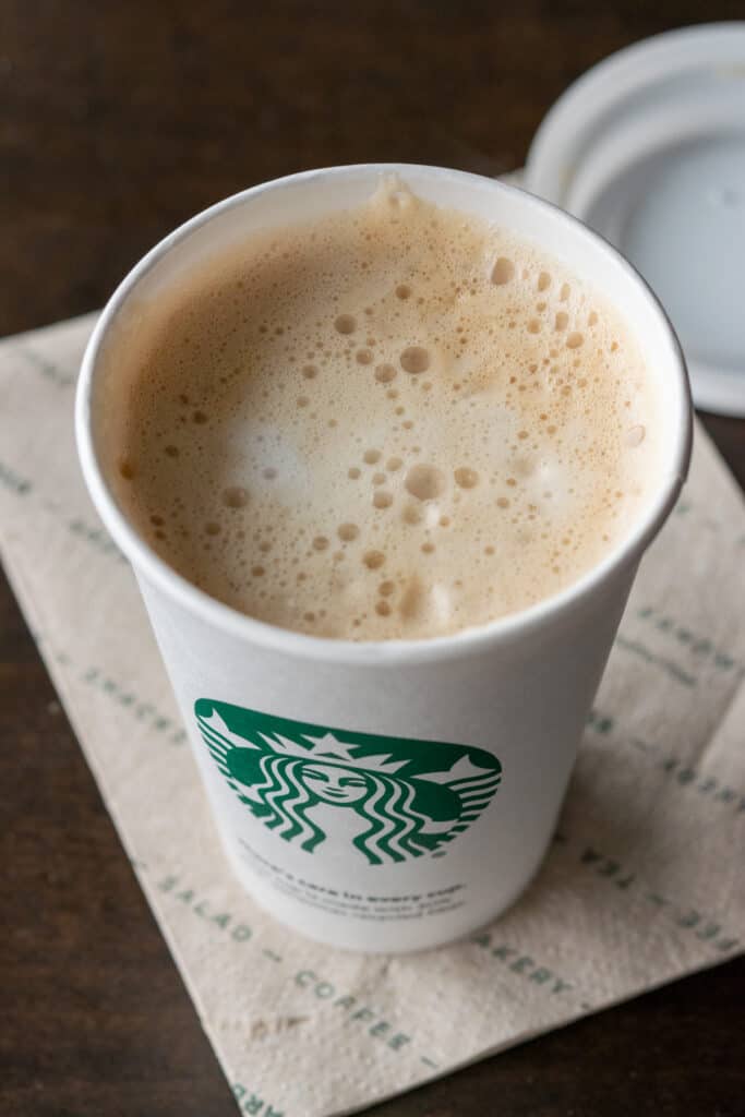 A creamy hot latte made with almond milk at Starbucks shown with the lid off.