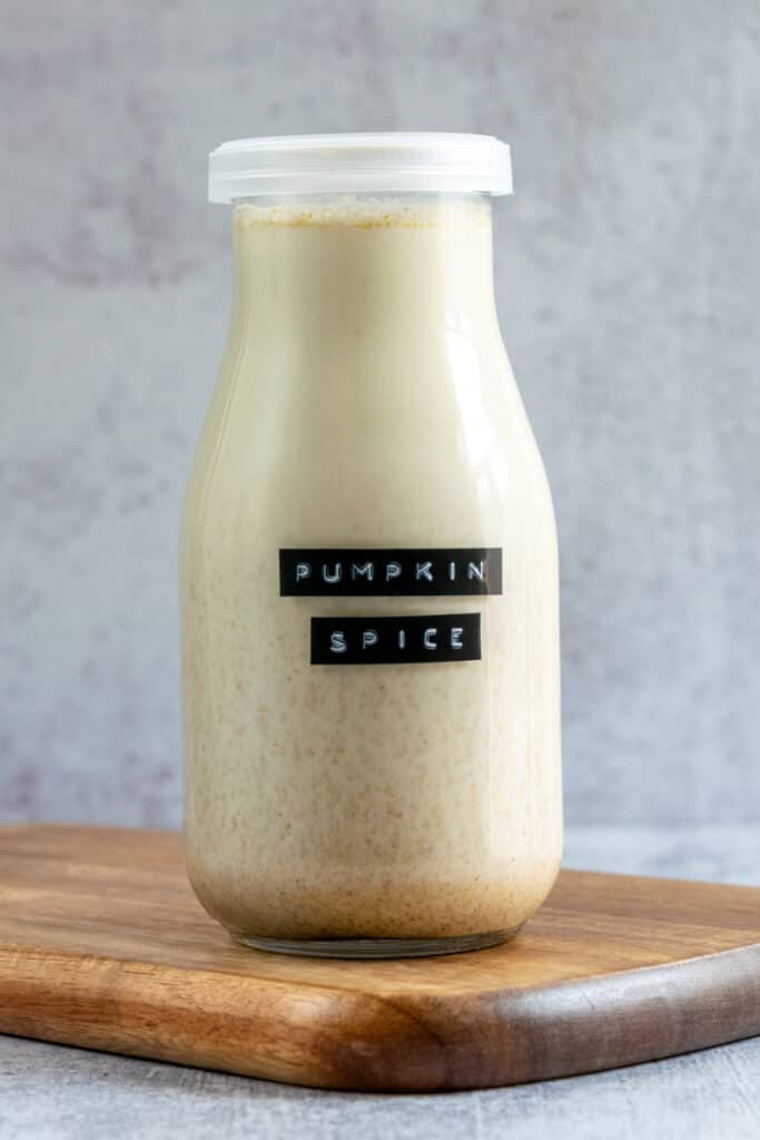 A milk bottle with a lid full of homemade pumpkin spice coffee creamer and a black embossed label on the glass bottle that says, pumpkin spice.