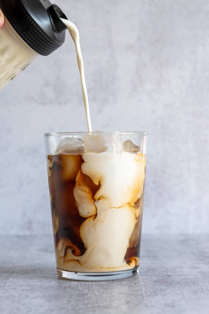 Italian Sweet Cream coffee creamer being poured into a glass of iced coffee.