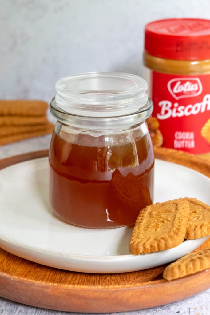 Bottle of homemade Biscoff cookie butter syrup, jar of Biscoff cookie butter spread and three speculoos cookies.
