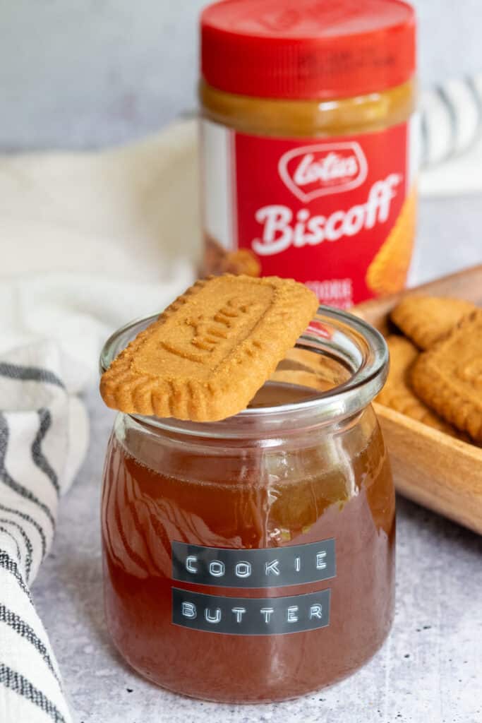 Lotus Biscoff cookie sitting on top of cookie butter syrup jar, with a jar of cookie butter spread in the background.