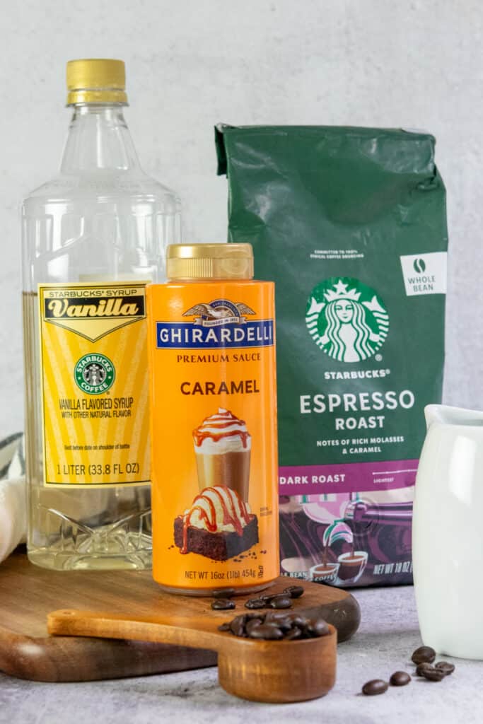 All the ingredients needed to make a caramel macchiato at home, including a bottle of vanilla syrup, bottle of caramel sauce, bag of Starbucks dark roast espresso beans and milk.