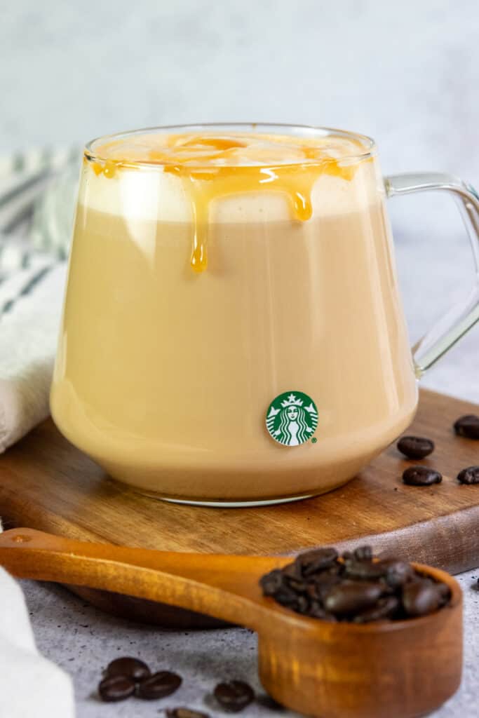 Homemade copycat Starbucks caramel macchiato with caramel sauce dripping down the side of a glass mug that has a Starbucks logo on it.