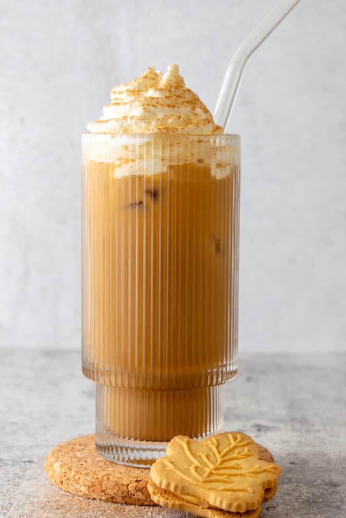An iced maple latte in a glass cup with glass straw and a maple syrup cookie sitting next to it.