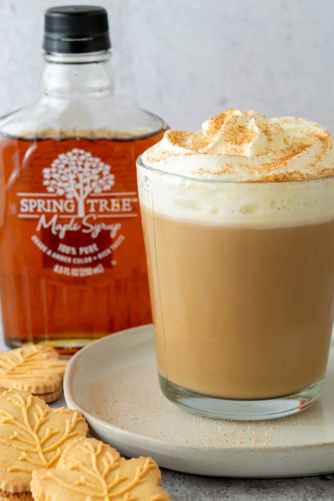 A bottle of pure maple syrup, maple leaf shaped cookies and a maple latte with whipped cream and cinnamon.