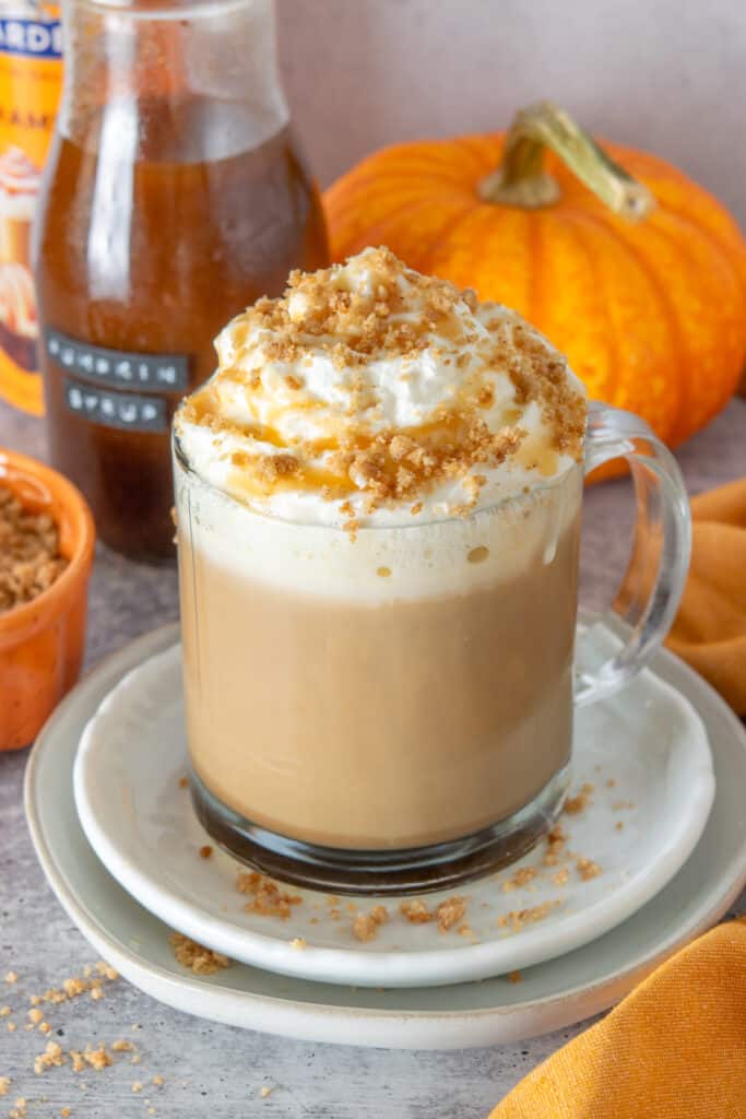 A big dollop of whipped cream on a pumpkin spice latte that's topped with butter pie crust crumbles and caramel sauce.