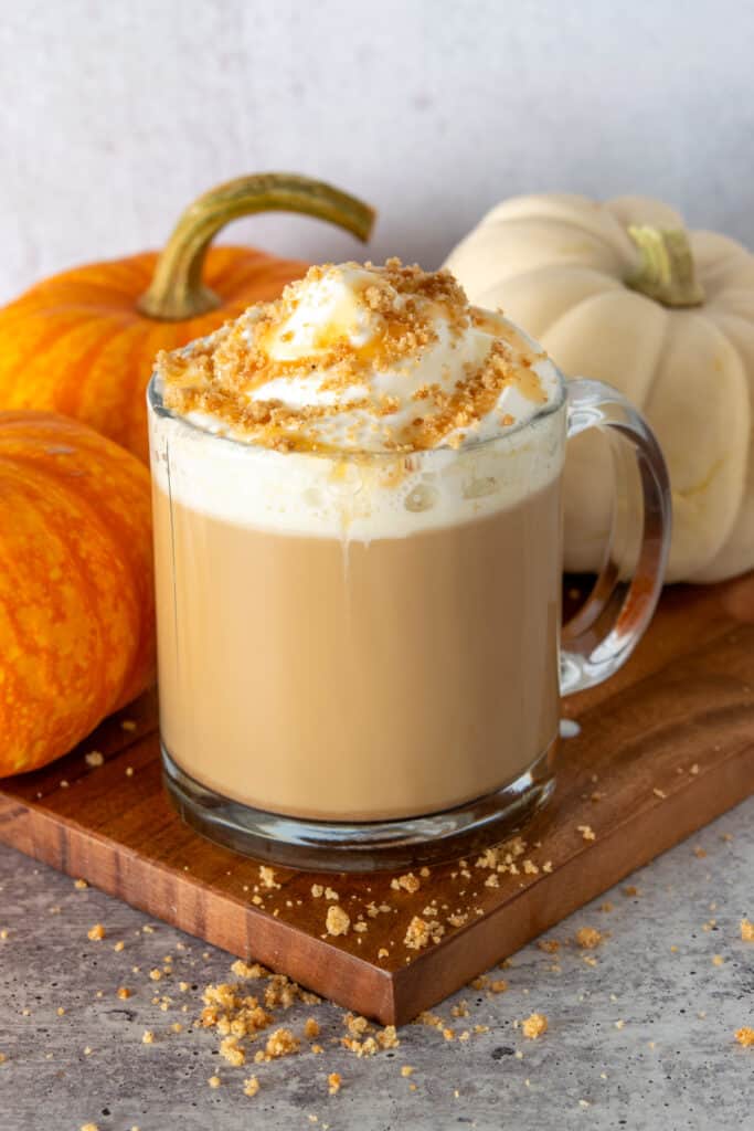 Homemade pumpkin pie latte in a mug sitting in front of three pumpkins.