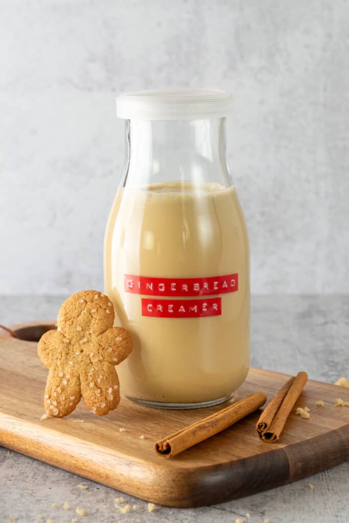 Bottle of homemade gingerbread coffee creamer with a gingerbread cookie and cinnamon sticks next to it.