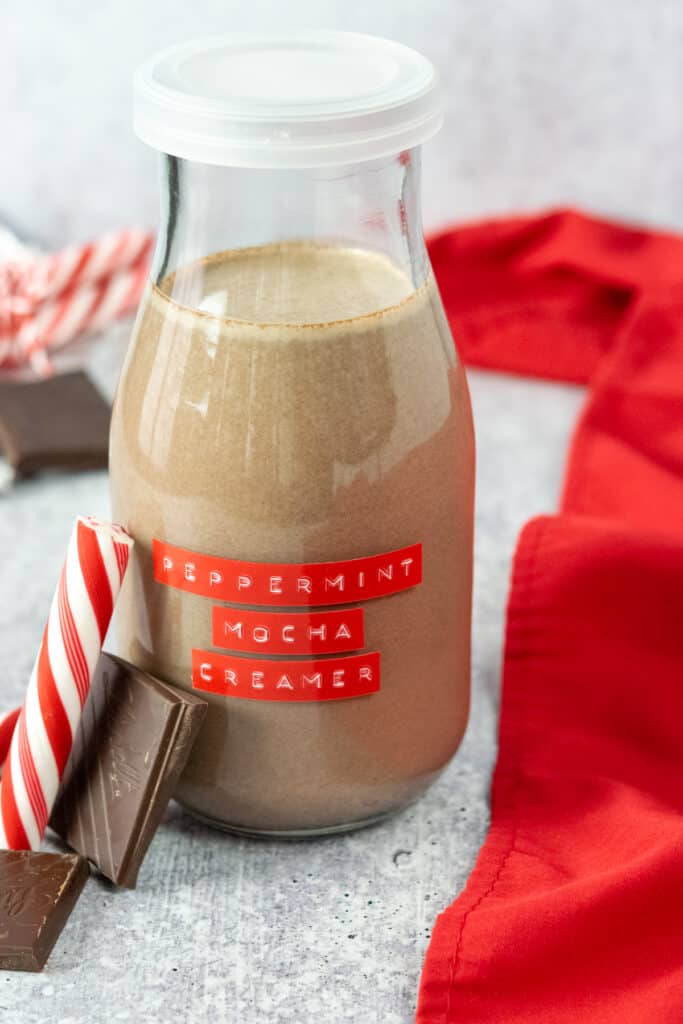 Jar of homemade peppermint mocha coffee creamer surrounded by peppermint sticks and pieces of dark cocoa.