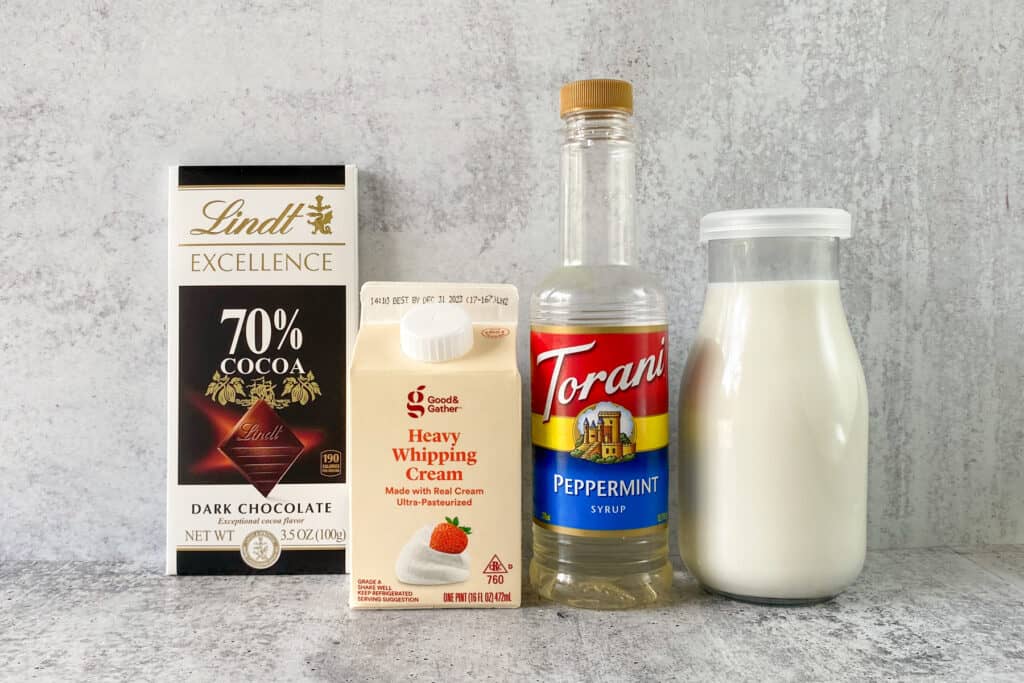 All the ingredients for making peppermint mocha coffee creamer in their packages, including Lindt 70% dark cocoa chocolate bar, carton of heavy whipping cream, bottle of Torani peppermint syrup and bottle of whole milk.