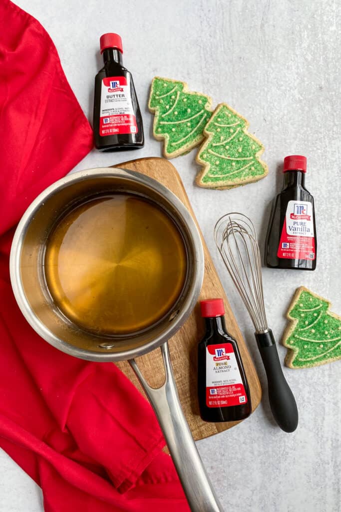 Simple syrup in a saucepan next to bottles of vanilla, almond and butter extracts.