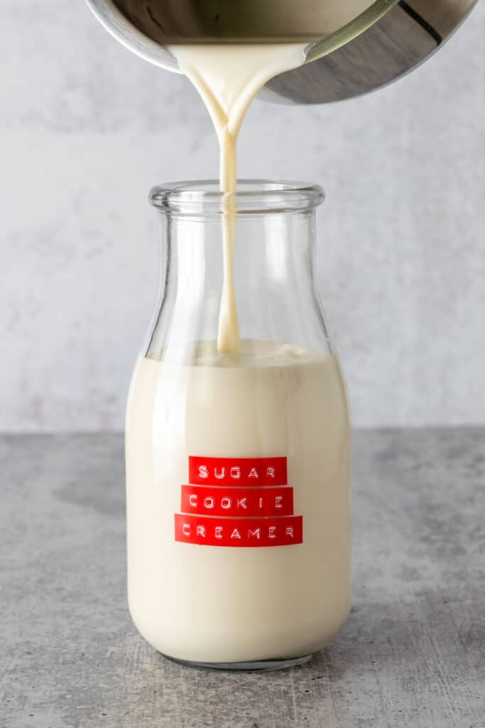 Pouring the creamer from the saucepan into a glass milk bottle that is labeled, sugar cookie creamer.