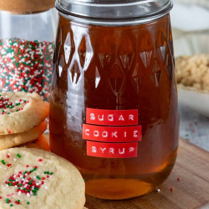 Homemade sugar cookie coffee syrup in a glass jar surrounded by sugar cookies.
