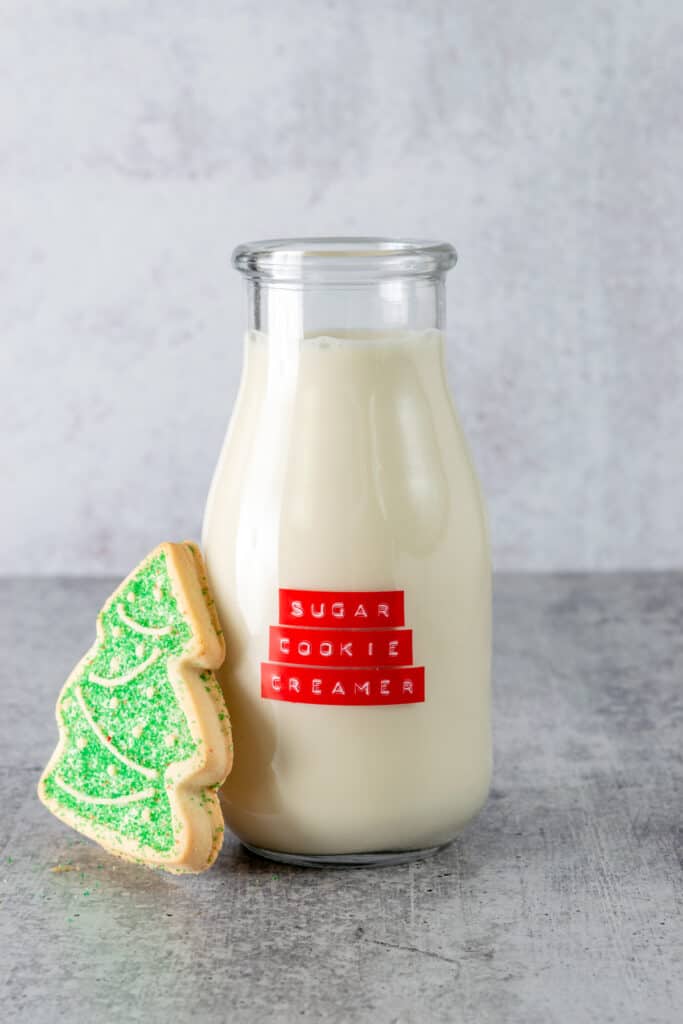 Christmas tree-shaped sugar cookie leaning against a bottle of homemade sugar cookie coffee creamer.