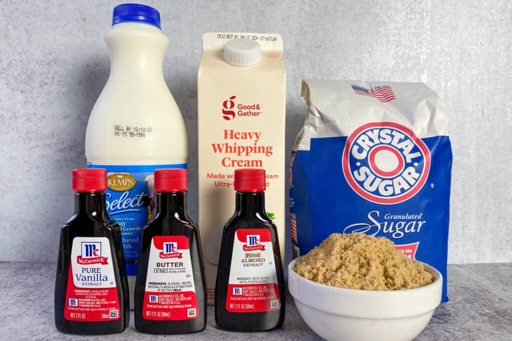 Three bottles of flavor extracts, milk, heavy whipping cream, granulated sugar and bowl of light brown sugar.