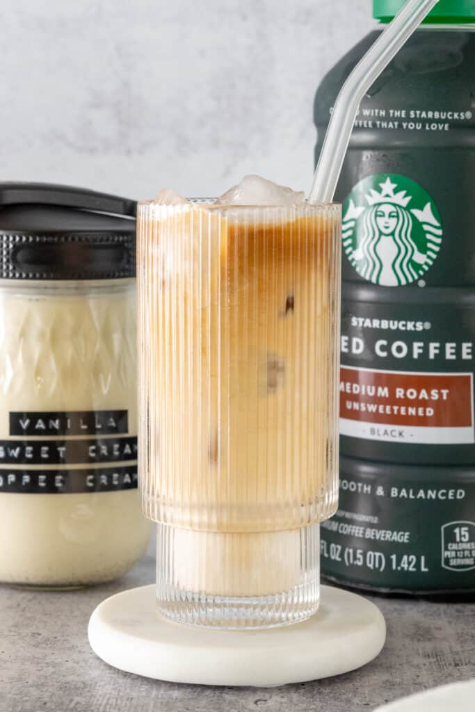 Glass of iced coffee with vanilla sweet cream in it, sitting in front of bottle of homemade vanilla sweet cream creamer and a bottle of Starbucks iced coffee.