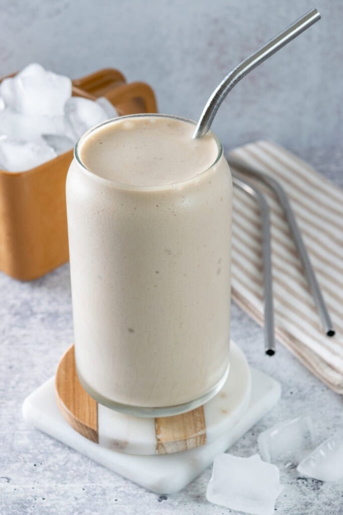 Blended frozen iced coffee in a glass next to a scoop of ice cubes.