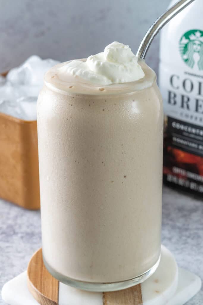 A creamy, slushy frozen iced coffee topped with a dollop of whipped cream in a cold glass with a straw in it.
