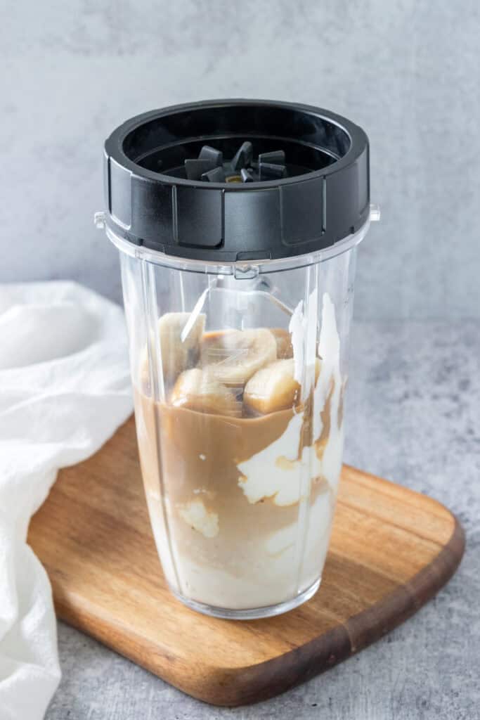 Ninja single-serve blender container with smoothie ingredients in it and lid with blades screwed on top.